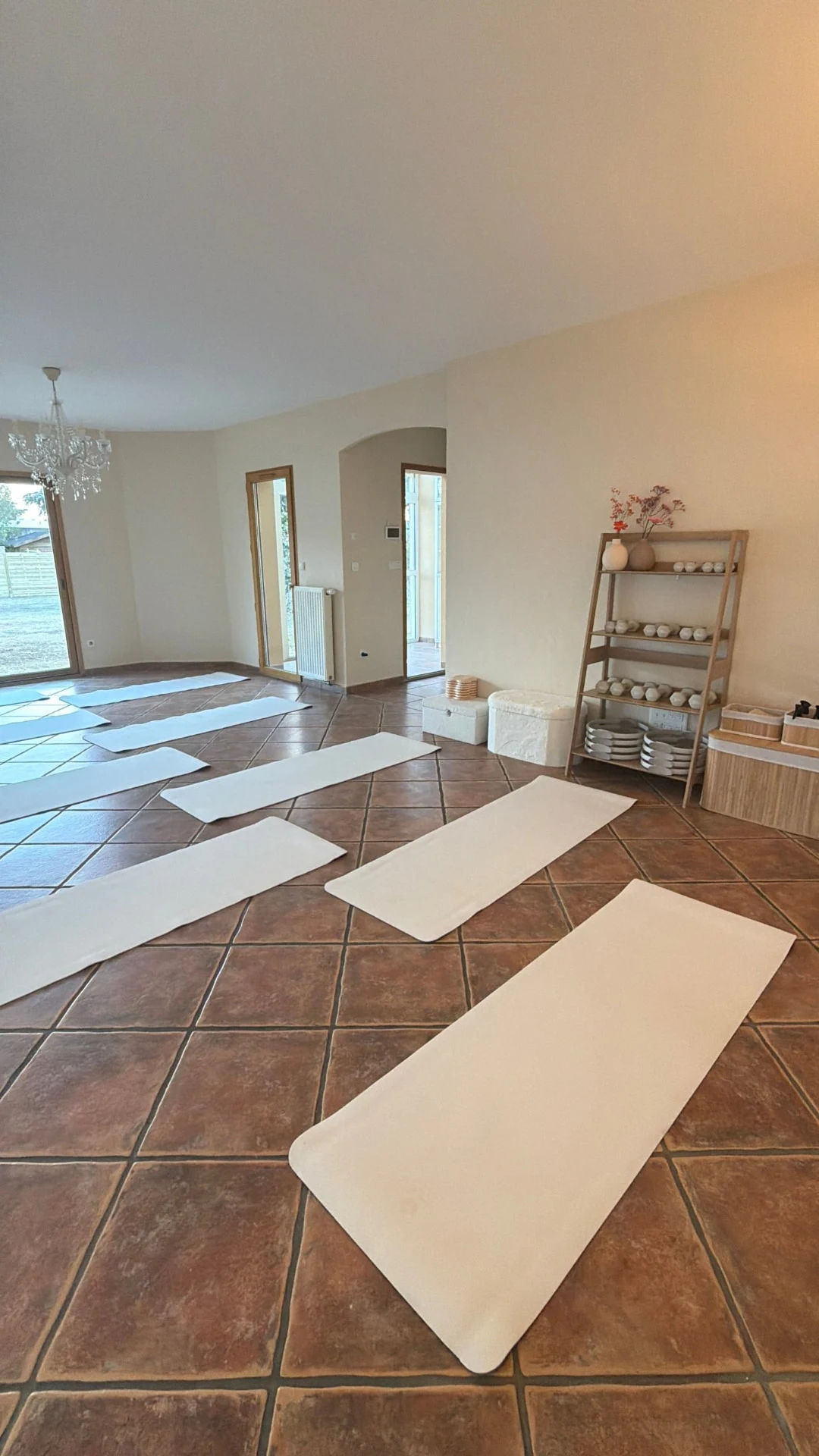 Vue du studio vers le jardin, avec tapis et matériel de Pilates rangé sur une étagère